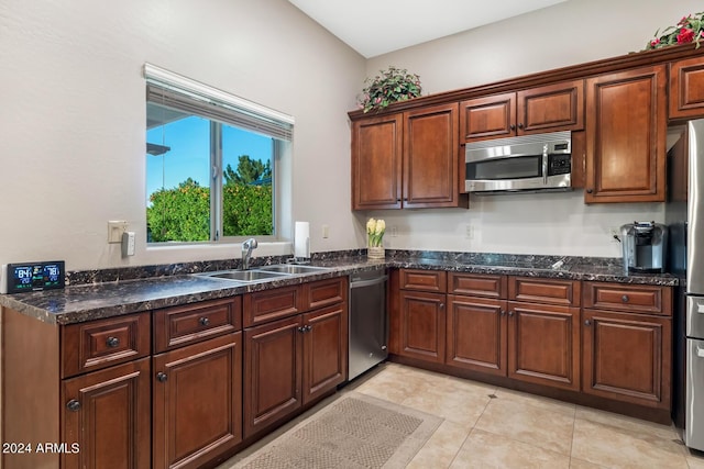 kitchen featuring a sink, light tile patterned floors, stainless steel appliances, and dark stone counters