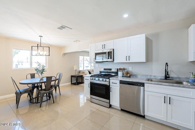 kitchen featuring sink, appliances with stainless steel finishes, light tile patterned floors, pendant lighting, and white cabinets