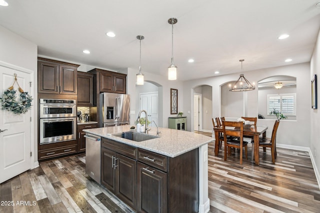 kitchen featuring sink, light stone counters, stainless steel appliances, dark brown cabinets, and a center island with sink