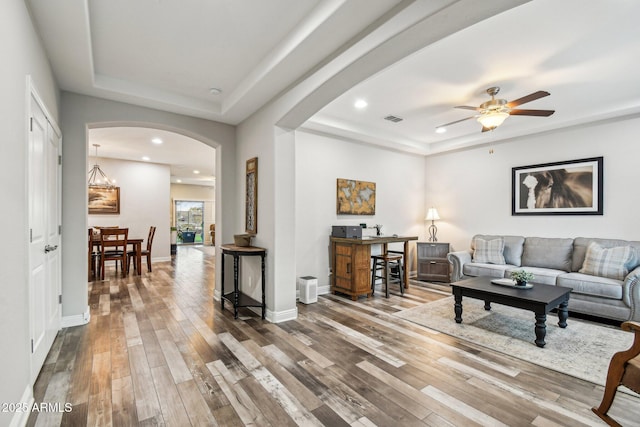 living room with a raised ceiling, hardwood / wood-style flooring, and ceiling fan