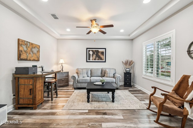 living room featuring hardwood / wood-style flooring, ceiling fan, and a raised ceiling