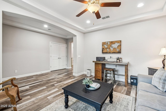 living room with ceiling fan, wood-type flooring, and a tray ceiling