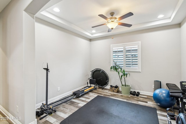 workout room featuring a tray ceiling, ceiling fan, and hardwood / wood-style flooring