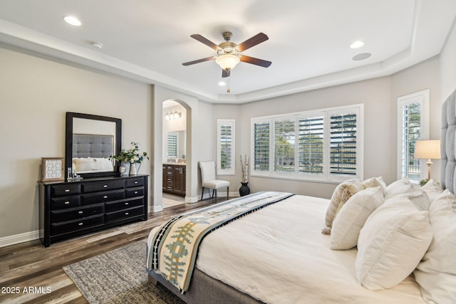 bedroom with ceiling fan, ensuite bath, dark hardwood / wood-style floors, and a raised ceiling