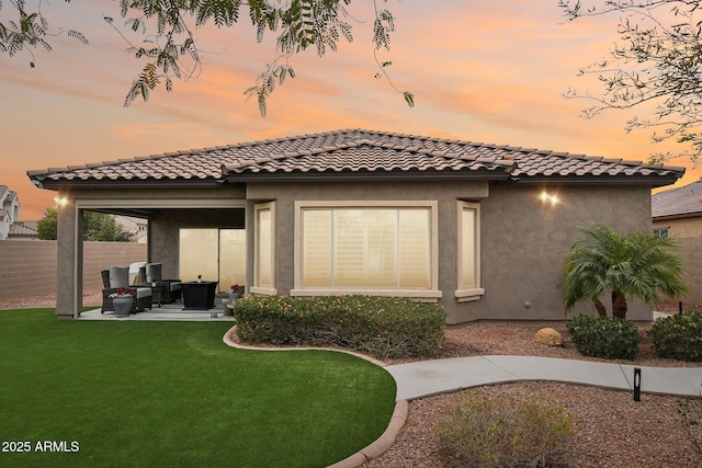 back house at dusk featuring a yard and a patio