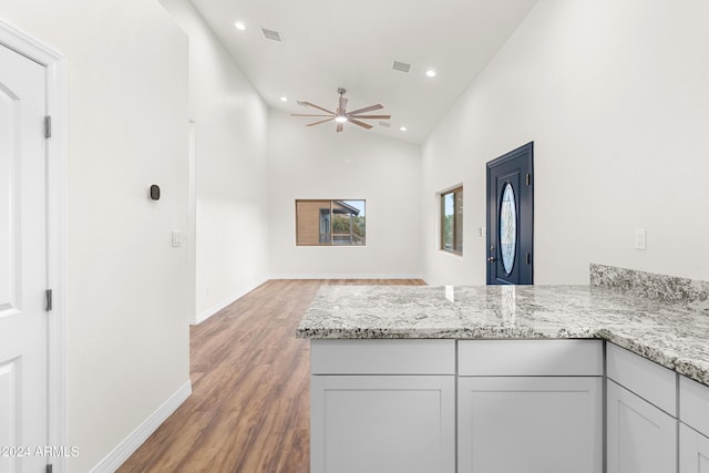 kitchen with white cabinetry, light stone countertops, hardwood / wood-style floors, and kitchen peninsula