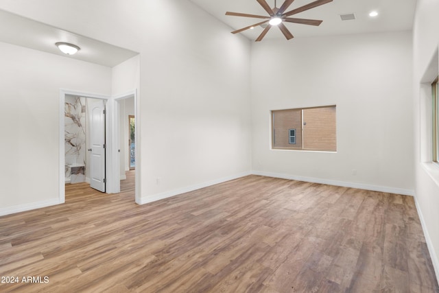 spare room with ceiling fan, light hardwood / wood-style flooring, and a towering ceiling