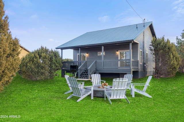 rear view of property with a wooden deck, a lawn, and an outdoor fire pit