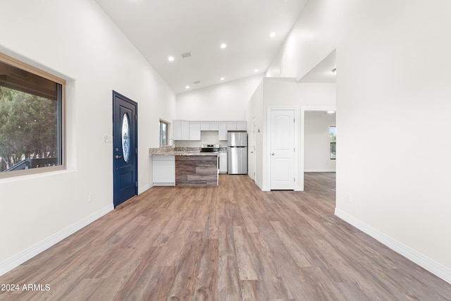 kitchen with stainless steel appliances, high vaulted ceiling, white cabinets, and light hardwood / wood-style floors