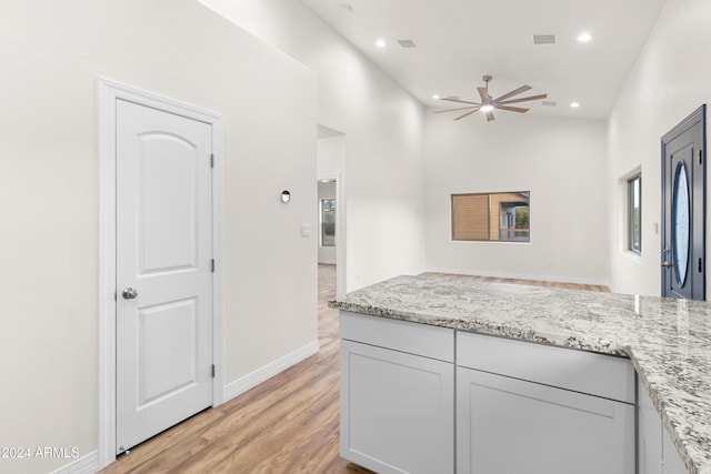 kitchen featuring ceiling fan, light stone countertops, and light wood-type flooring