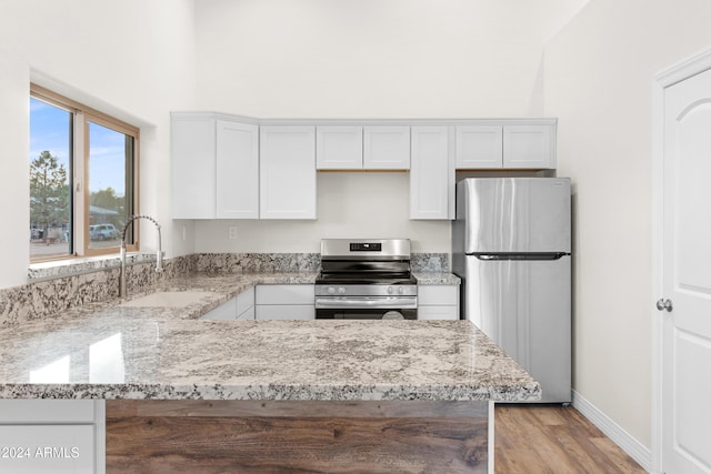 kitchen with sink, light stone counters, light wood-type flooring, appliances with stainless steel finishes, and white cabinets