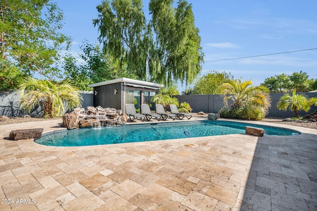 view of pool with pool water feature, a patio, and an outbuilding