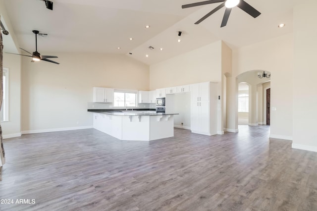 kitchen featuring white cabinets, light hardwood / wood-style floors, oven, high vaulted ceiling, and built in microwave