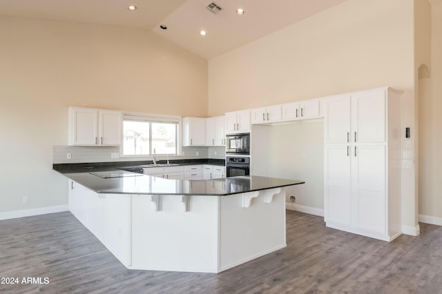 kitchen with kitchen peninsula, built in microwave, white cabinetry, high vaulted ceiling, and stainless steel oven