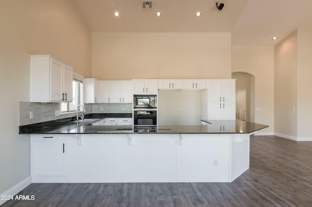 kitchen featuring kitchen peninsula, sink, white cabinetry, a towering ceiling, and black appliances