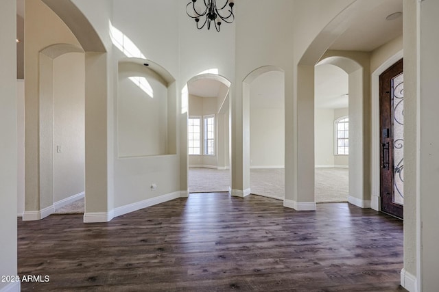 entryway with a high ceiling, a notable chandelier, a healthy amount of sunlight, and dark wood-type flooring