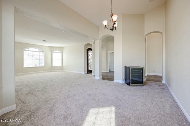 unfurnished living room with carpet floors, beverage cooler, and an inviting chandelier