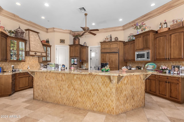 kitchen featuring custom range hood, a large island with sink, built in appliances, and crown molding