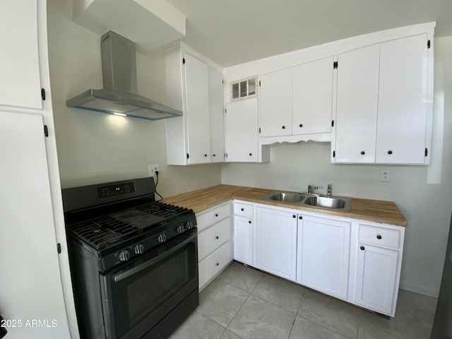 kitchen featuring black gas range oven, wall chimney range hood, sink, white cabinetry, and light tile patterned flooring