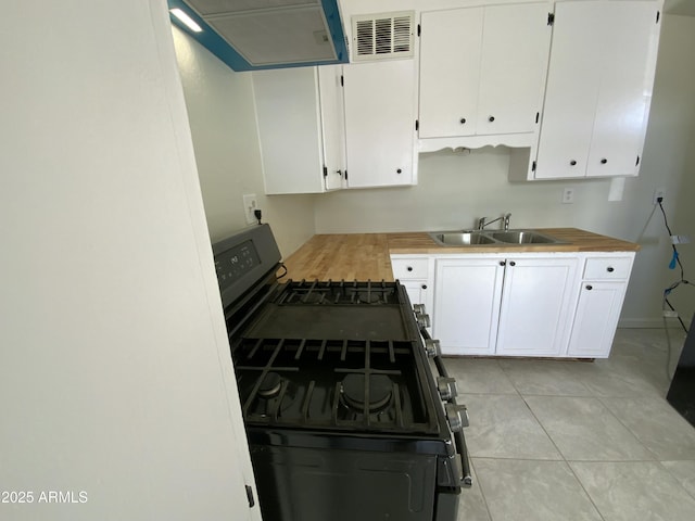 kitchen with light tile patterned flooring, butcher block counters, sink, black gas range oven, and white cabinets