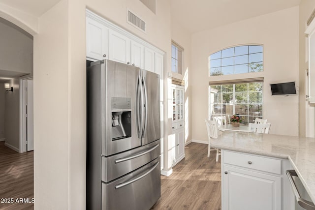 kitchen with white cabinets, stainless steel fridge with ice dispenser, light wood-type flooring, and light stone counters