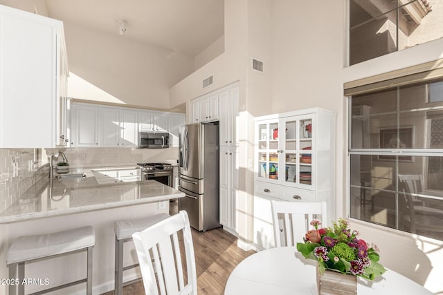 kitchen with stainless steel appliances, sink, white cabinetry, kitchen peninsula, and a high ceiling