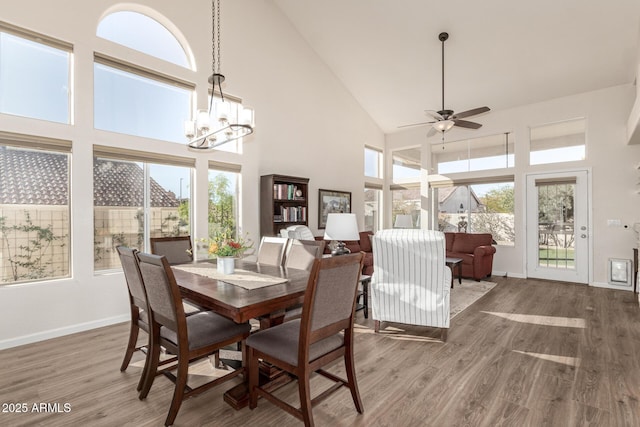 dining space with a towering ceiling, hardwood / wood-style flooring, and ceiling fan with notable chandelier