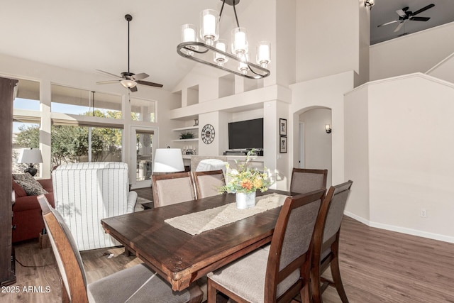 dining area with hardwood / wood-style floors, built in features, a towering ceiling, and ceiling fan with notable chandelier