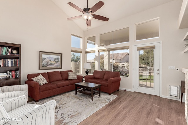 living room featuring a high ceiling, a stone fireplace, ceiling fan, and light hardwood / wood-style flooring