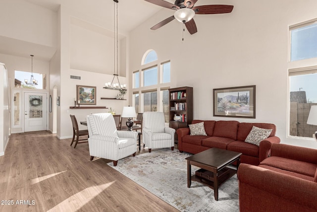 living room with a towering ceiling, ceiling fan with notable chandelier, a healthy amount of sunlight, and light hardwood / wood-style flooring