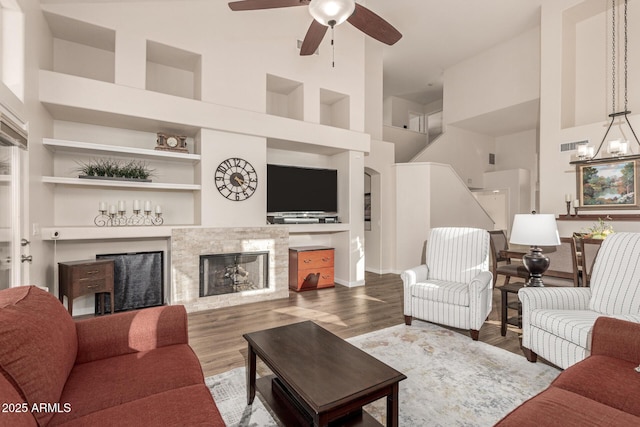 living room featuring a towering ceiling, wood-type flooring, ceiling fan with notable chandelier, and built in shelves