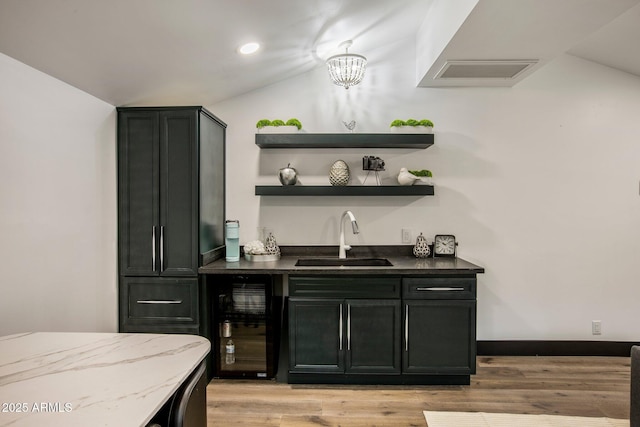 bar with wine cooler, sink, a notable chandelier, and light hardwood / wood-style flooring