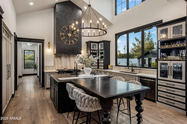 kitchen with wood-type flooring, sink, stainless steel dishwasher, and a towering ceiling