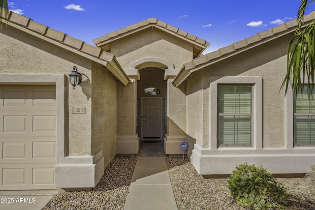 entrance to property with stucco siding, a tiled roof, and a garage