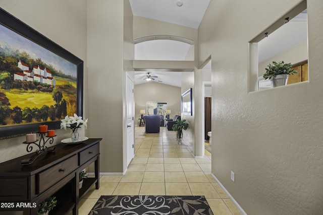 corridor featuring baseboards, light tile patterned floors, a textured wall, and vaulted ceiling