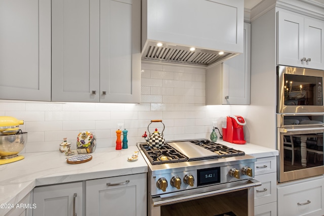 kitchen with tasteful backsplash, white cabinets, custom exhaust hood, light stone counters, and stainless steel appliances