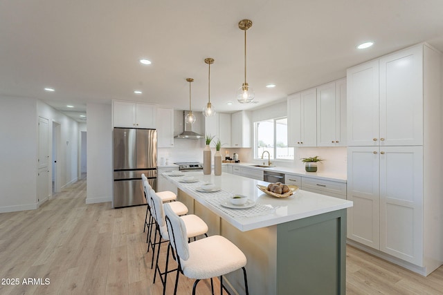 kitchen featuring stainless steel appliances, white cabinetry, a sink, a kitchen island, and wall chimney exhaust hood