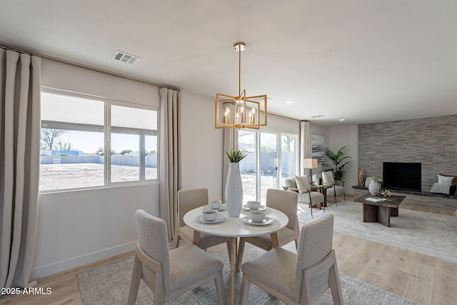 dining area featuring a notable chandelier, a fireplace, visible vents, baseboards, and light wood-type flooring