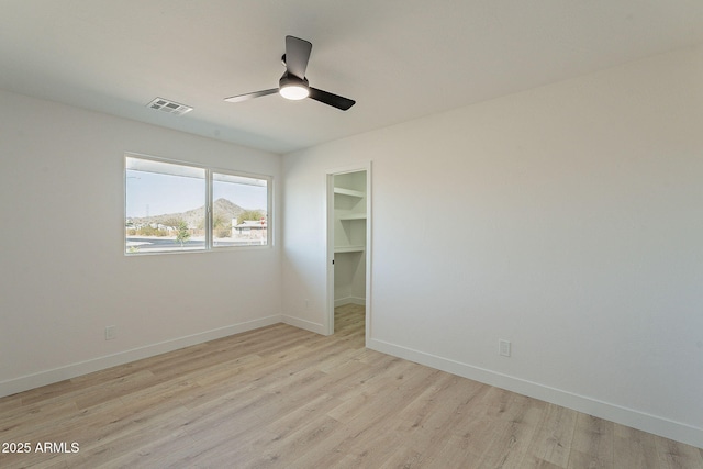 spare room featuring light wood-style flooring, a ceiling fan, visible vents, and baseboards