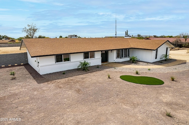 ranch-style home featuring driveway, roof with shingles, fence, and brick siding