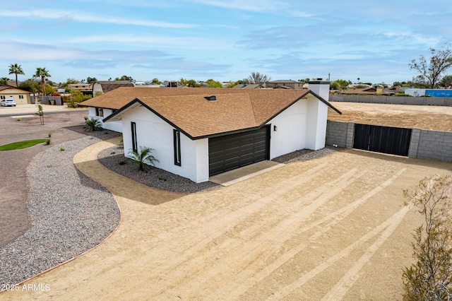 view of front of house featuring roof with shingles, brick siding, dirt driveway, fence, and a garage