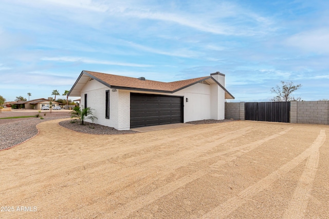 garage featuring a gate, fence, and dirt driveway