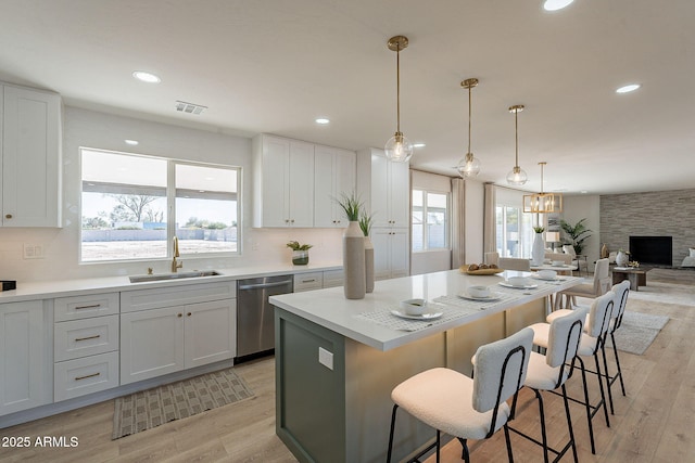 kitchen with a breakfast bar, light wood finished floors, visible vents, stainless steel dishwasher, and a sink