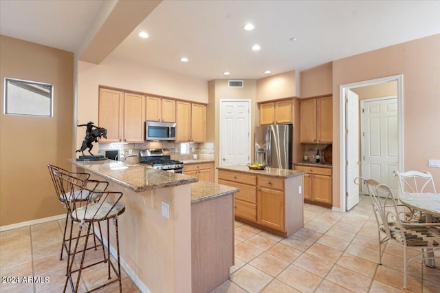 kitchen with light stone counters, light brown cabinets, kitchen peninsula, appliances with stainless steel finishes, and decorative backsplash