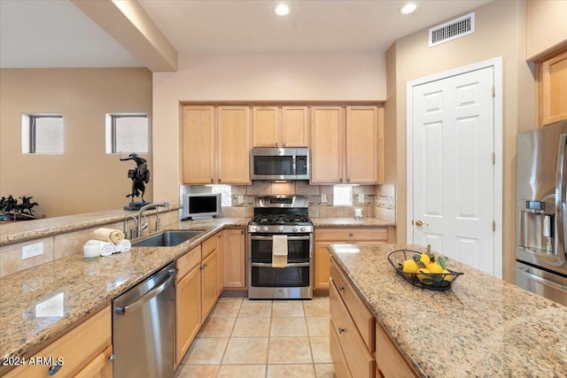 kitchen with light brown cabinetry, light stone counters, appliances with stainless steel finishes, and sink