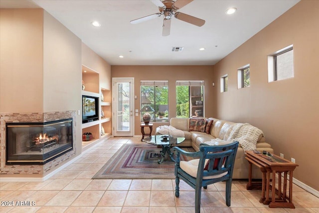 tiled living room featuring ceiling fan, a stone fireplace, and built in shelves