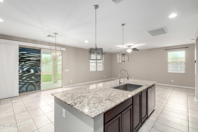 kitchen featuring sink, light tile patterned floors, dark brown cabinetry, light stone counters, and decorative light fixtures