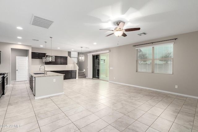 kitchen with ceiling fan with notable chandelier, pendant lighting, sink, a kitchen island with sink, and light stone counters