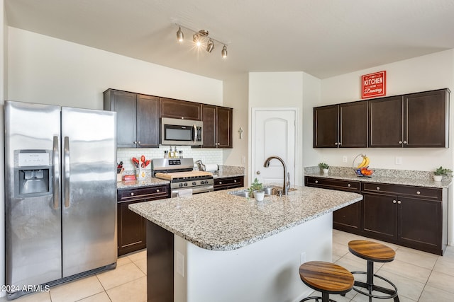 kitchen with tasteful backsplash, an island with sink, sink, light stone countertops, and appliances with stainless steel finishes