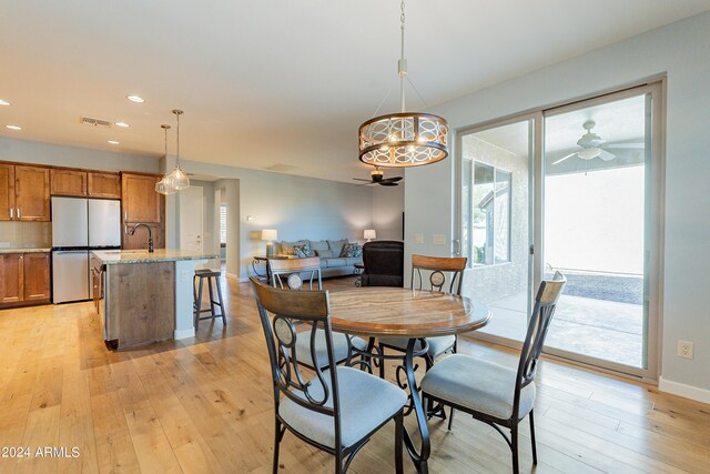 dining area with light wood-type flooring, ceiling fan with notable chandelier, and sink